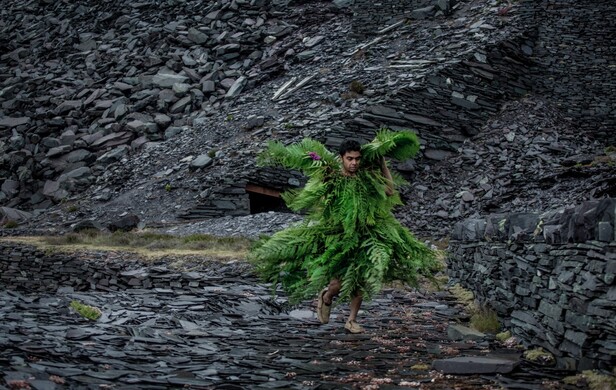 A man walking through a slate mine dressed in a costume made from bright green ferns.
