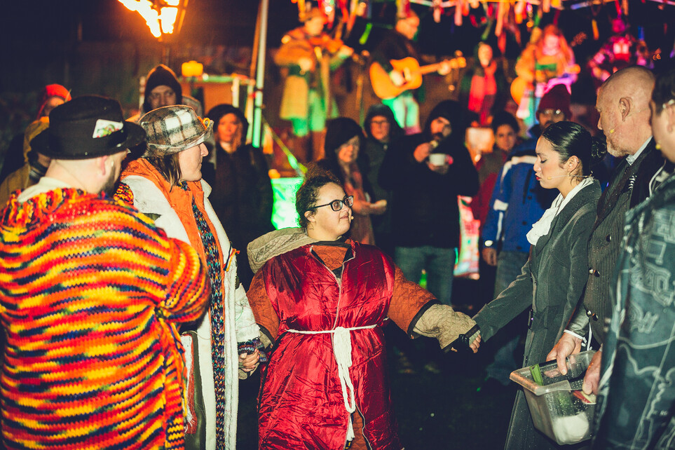 A group of people representing different ages and abilities stand in a group. Two are holding hands.