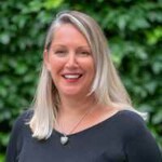 Unigolyn â gwallt melyn hir, yn gwisgo top du ac yn gwenu ar y camera.