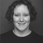 Unigolyn â gwallt cyrliog byr dywyll. Maen nhw'n gwisgo crys-t du ac yn gwenu'n uniongyrchol ar y camera. Mae'r llun mewn du a gwyn.