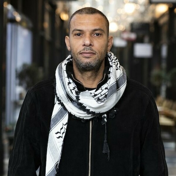 Kyle is wearing a black jacket with a black and white scarf around his neck